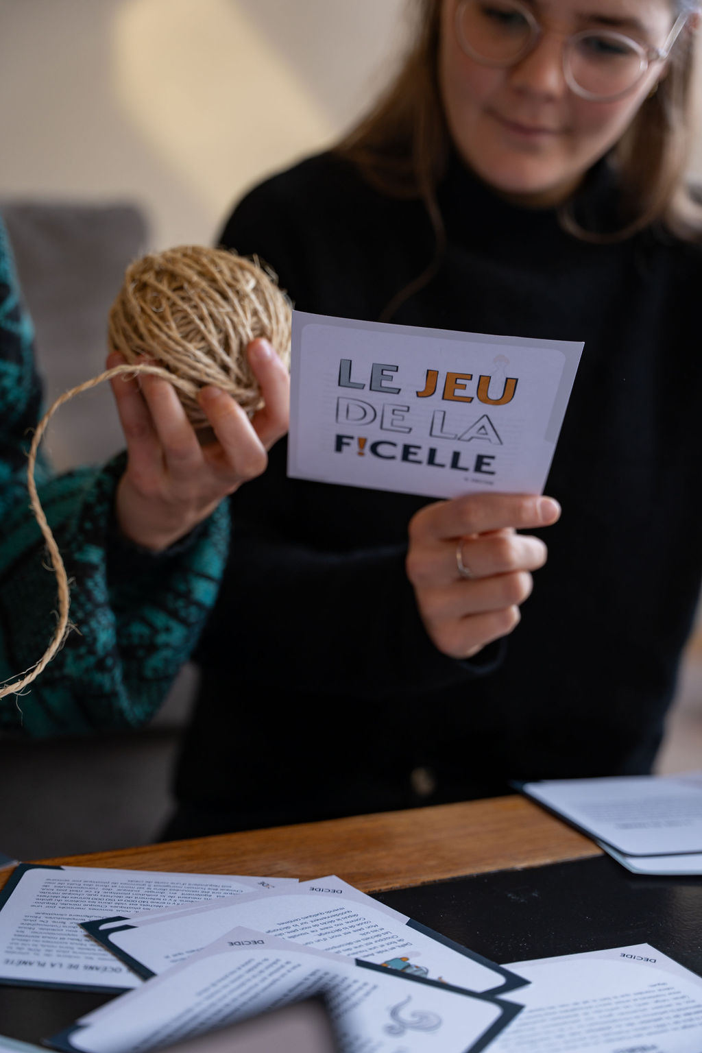Gros plan sur le Jeu de la Ficelle : pelote de ficelle et carte d’atelier en mains